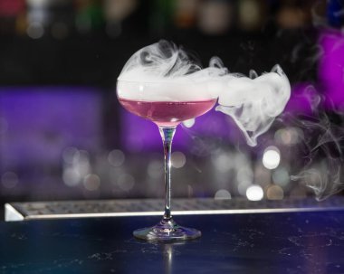 Coupe bardağındaki bu görsel olarak çarpıcı pembe alkollü kokteyl etrafında daha fazla duman dalgası olan büyük bir kokteyl içeriyor..