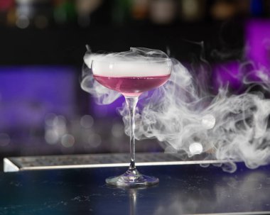 Coupe bardağındaki bu görsel olarak çarpıcı pembe alkollü kokteyl etrafında daha fazla duman dalgası olan büyük bir kokteyl içeriyor..