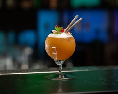 ibrant turuncu alkollü kokteyl, eşsiz yuvarlak bardakta servis edilir, bir sapla, nane, böğürtlen ve iki pipetle süslenir, hepsi bir bar tezgahına kurulur..