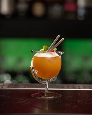 ibrant turuncu alkollü kokteyl, eşsiz yuvarlak bardakta servis edilir, bir sapla, nane, böğürtlen ve iki pipetle süslenir, hepsi bir bar tezgahına kurulur..