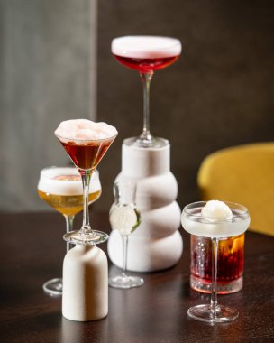 Renk ve sunum olarak değişen beş farklı alkollü kokteyl koleksiyonu bulanık bir arka plana karşı sanatsal bir şekilde karanlık bir masada düzenlenmiştir. .