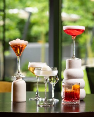 Renk ve sunum olarak değişen beş farklı alkollü kokteyl koleksiyonu bulanık bir arka plana karşı sanatsal bir şekilde karanlık bir masada düzenlenmiştir. .