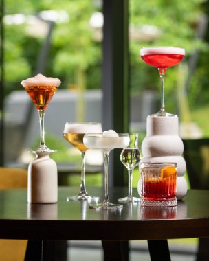 Renk ve sunum olarak değişen beş farklı alkollü kokteyl koleksiyonu bulanık bir arka plana karşı sanatsal bir şekilde karanlık bir masada düzenlenmiştir. .