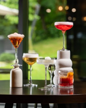 Renk ve sunum olarak değişen beş farklı alkollü kokteyl koleksiyonu bulanık bir arka plana karşı sanatsal bir şekilde karanlık bir masada düzenlenmiştir. .