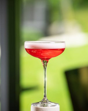 Beyaz köpüklü, canlı bir pembe kokteyl beyaz desenli bir ayakta mükemmel bir şekilde dengelenmiştir. Parlak, yeşil, bulanık bir arka plan üzerine kuruludur.