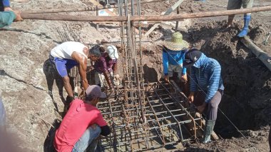 İnşaat alanındaki işçiler vakfın demir çerçevesini elle kaldırmak için birlikte çalışırlar.