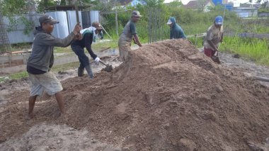 İşçiler elle toprağı çapalarla döker ve düzleştirirler.