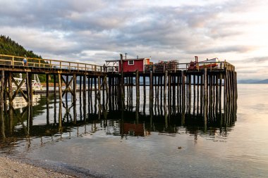 HOONAH, ALASKA, USA - AUGUST 16, 2021:  A fishing pier at dusk in Icy Strait Point, a popular cruise ship port in Alaska. clipart