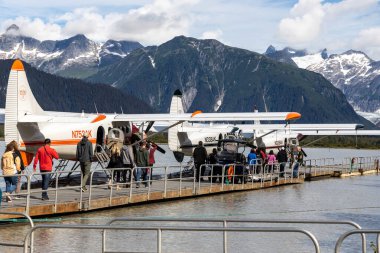 JUNEAU, ALASKA, ABD - 19 Ağustos 2022: Bir grup turist tarihi Taku Lodge 'da arka planda buzul dağlarıyla birlikte yüzen uçaklara bindi.