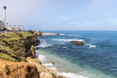 Deniz kabuğu plajı, La Jolla, California 'da, arka planda La Jolla Çocuk Havuzu ve cankurtaran istasyonu var..