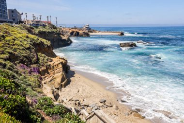 Deniz kabuğu plajı, La Jolla, California 'da, arka planda La Jolla Çocuk Havuzu ve cankurtaran istasyonu var..