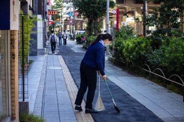 Tokyo, Japonya, 26 Ekim 2023: Şehir Caddesindeki kaldırımı süpüren işçi