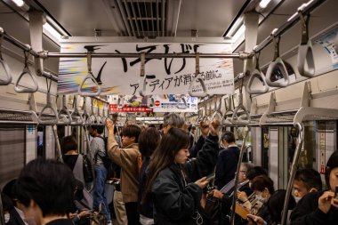Tokyo, Japonya, 26 Ekim 2023: Akıllı telefon kullanan yolcularla dolu kalabalık bir metro treni görüntüsü