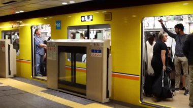 Tokyo, Japonya, 22 Kasım 2023: Sarı bir metro trenine binen banliyö yolcuları