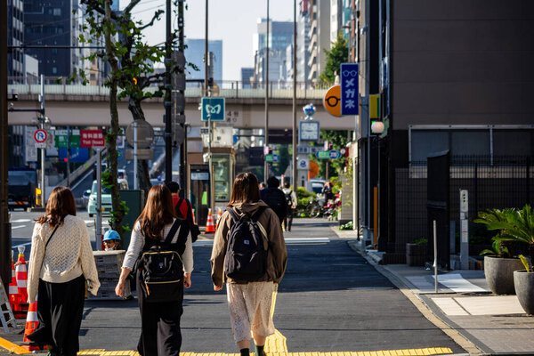 Tokyo, Japan, 27 November 2023: Three People Walking on City Sidewalk Near Roadworks