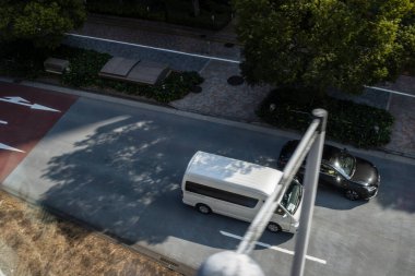 Şehir caddesinde park etmiş beyaz bir minibüs ve arabaların hava görüntüsü.