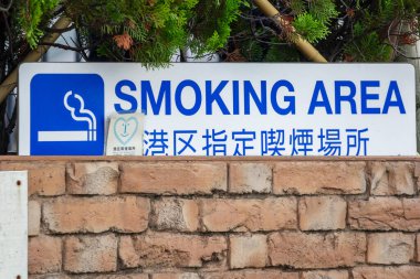 Tokyo, Japonya, 27 Ekim 2023: Ağaçlı tuğla bir duvara karşı sigara içme alanı tabelası
