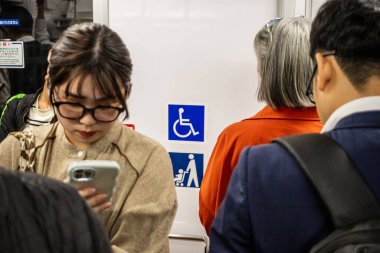 Tokyo, Japonya, 27 Ekim 2023: Tokyo metrosunda akıllı telefon kullanan genç kadın