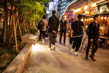 Tokyo, Japonya, 27 Ekim 2023: Canlı bir mahallede gece birlikte yürüyen bir grup arkadaş