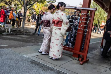 Tokyo, Japonya, 28 Ekim 2023: Geleneksel kimonolu iki kadın bir tapınakta rehber direğine danışıyor.