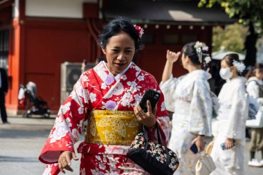 Tokyo, Japonya, 28 Ekim 2023: Kırmızı kimonolu kadın tapınakta el çantası taşıyor