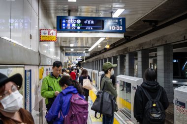 Tokyo, Japonya, 29 Ekim 2023: Dijital zaman çizelgesine sahip metro istasyonunda seyahat edenler