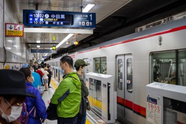 Tokyo, Japonya, 29 Ekim 2023: Metro treni bekleyen yolcularla istasyona varıyor.