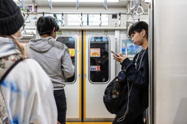 Tokyo, Japonya, 30 Ekim 2023: Tokyo metrosunda akıllı telefon kullanan banliyö çalışanı