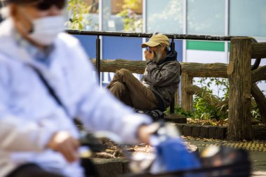 Tokyo, Japonya, 30 Ekim 2023: Yaşlı adam akıllı telefon kullanırken bankta oturuyor