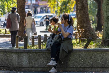 Tokyo, Japonya, 30 Ekim 2023: Genç bir kadın park çıkıntısında otururken öğle yemeği yiyor