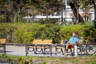 Tokyo, Japonya, 30 Ekim 2023: Huzurlu bir park ortamında halka açık bir bankta oturan adam