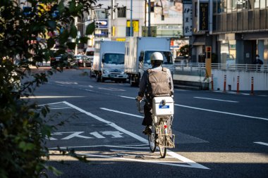 Tokyo, Japonya, 30 Ekim 2023: Güneşli bir caddede mal teslimatı yapan bisikletçi