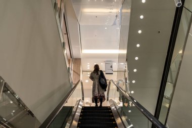Tokyo, Japonya, 30 Ekim 2023: Tokyo 'da modern bir alışveriş merkezinde yürüyen merdivene binen kadın