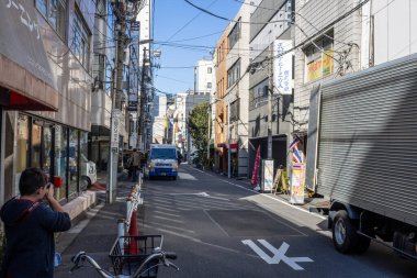 Tokyo, Japonya, 30 Ekim 2023: Kalabalık bir caddeyi dükkanlar ve geçen bir kamyonla fotoğraflayan adam