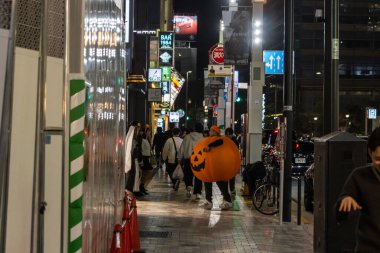 Tokyo, Japonya, 31 Ekim 2023: Geceleri insanlar balkabağı kostümlü biriyle sokakta yürüyorlar