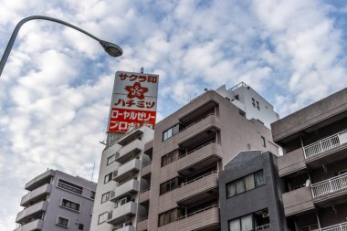 Tokyo, Japonya, 31 Ekim 2023: Bulutlu bir gökyüzüne karşı belirgin kırmızı ve beyaz tabelalı şehir binaları