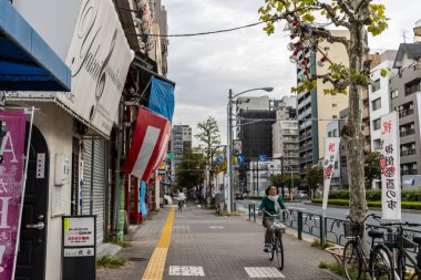 Tokyo, Japonya, 31 Ekim 2023: Kapalı dükkanlardan geçen bir bisikletçiyle Tokyo caddesinde sakin bir sabah