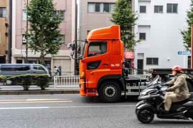 Tokyo, Japonya, 31 Ekim 2023: Parlak turuncu bir kamyon ve motosikletli bir trafik sahnesi