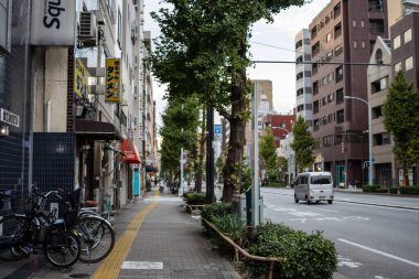 Tokyo, Japonya, 31 Ekim 2023: Park etmiş bisikletleri ve geçen arabasıyla Sessiz Tokyo Caddesi