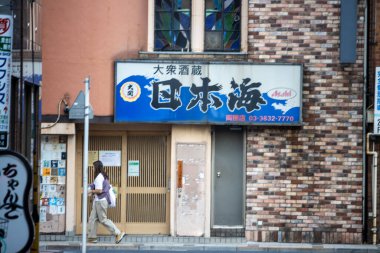 Tokyo, Japonya, 1 Kasım 2023: Kapalı bir dükkanın önünden geleneksel Japon tabelasıyla geçen yayalar