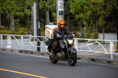 Tokyo, Japonya, 1 Kasım 2023: Motosikletli bir teslimatçı köprüden geçiyor