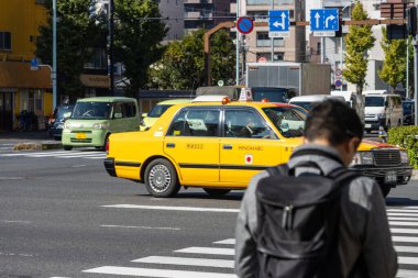 Tokyo, Japonya, 1 Kasım 2023: İkonik sarı Tokyo taksisi ve yayalar ile hareketli sokak sahnesi