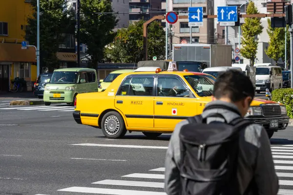 Tokyo, Japonya, 1 Kasım 2023: İkonik sarı Tokyo taksisi ve yayalar ile hareketli sokak sahnesi
