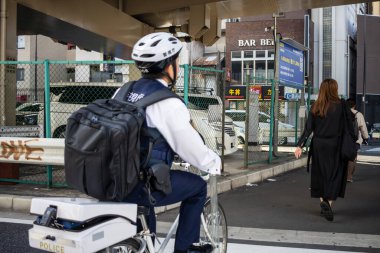 Tokyo, Japonya, 2 Kasım 2023: Bisikletli polis şehir ortamında yayaları gözlemliyor