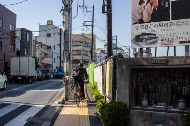 Tokyo, Japonya, 2 Kasım 2023: Arka planda reklam panosu olan bir Tokyo caddesinde bisiklet süren adam