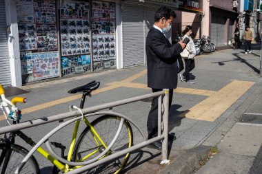 Tokyo, Japonya, 2 Kasım 2023: Tokyo 'da kapalı dükkanların yakınında akıllı telefon kullanan adam