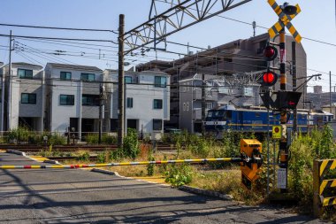 Tokyo, Japonya, 3 Kasım 2023: Bir yerleşim bölgesinde uyarı ışıkları ve bariyerler ile tren geçişi