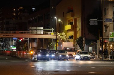 Tokyo, Japonya, 3 Kasım 2023: Araçlar ve yaya köprüsü olan bir cadde kavşağının gece görüntüsü