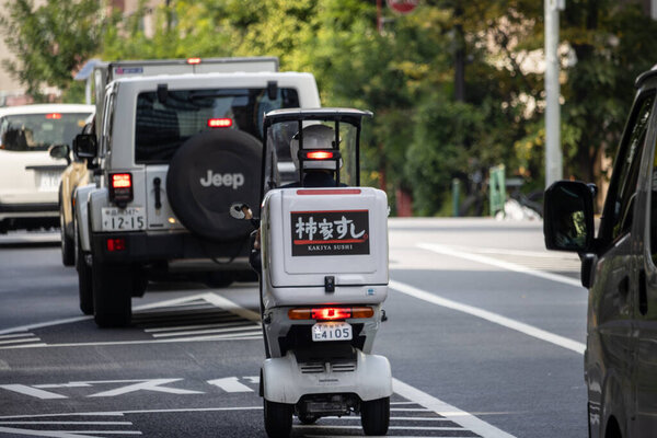 Tokyo, Japan, 4 November 2023: Sushi Delivery Scooter Navigating Through Tokyo Traffic