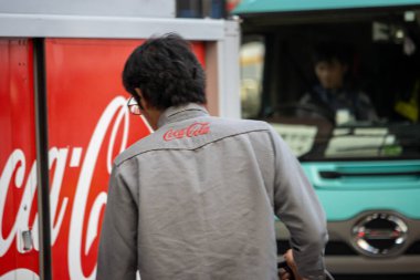 Tokyo, Japonya, 4 Kasım 2023: Coca-Cola logosu olan ceketli adam bir otobüsün yanında duruyor